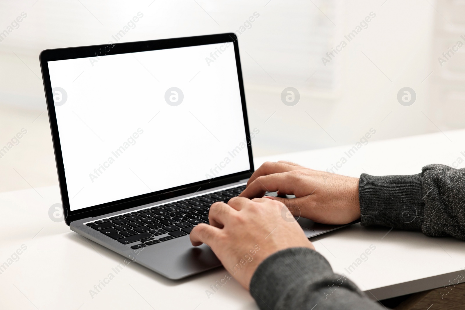 Photo of E-learning. Young man using laptop at white table, closeup