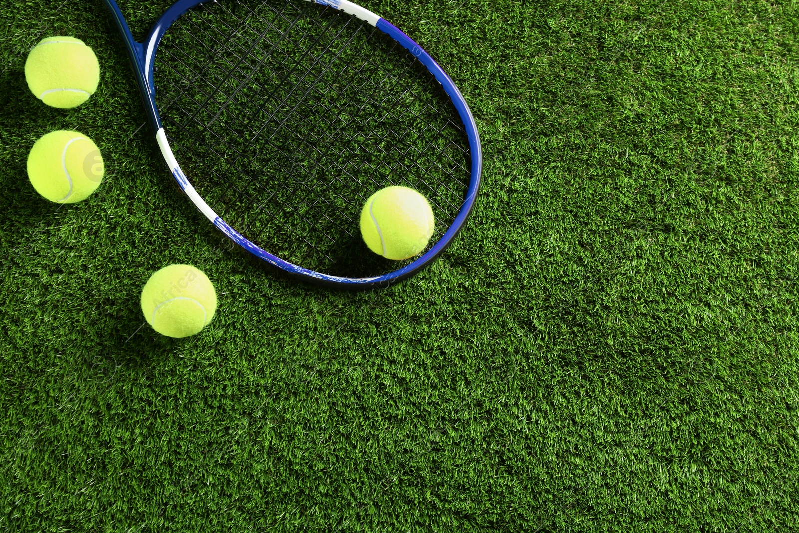 Photo of Tennis racket and balls on green grass, flat lay. Space for text