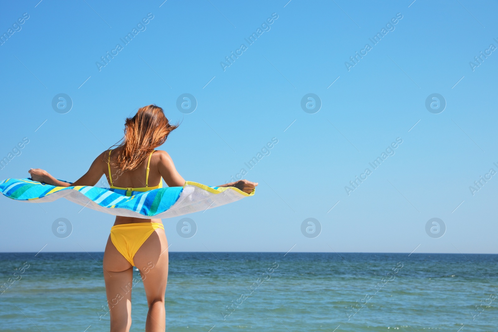 Photo of Woman with beach towel near sea on sunny day, back view