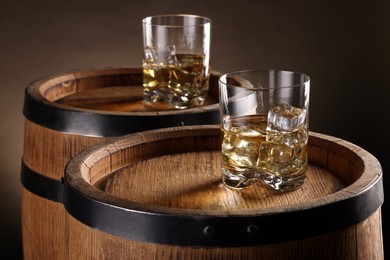 Photo of Whiskey with ice cubes in glasses on wooden barrels against dark background, closeup