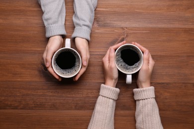 Photo of Women with cups of coffee at wooden table, top view