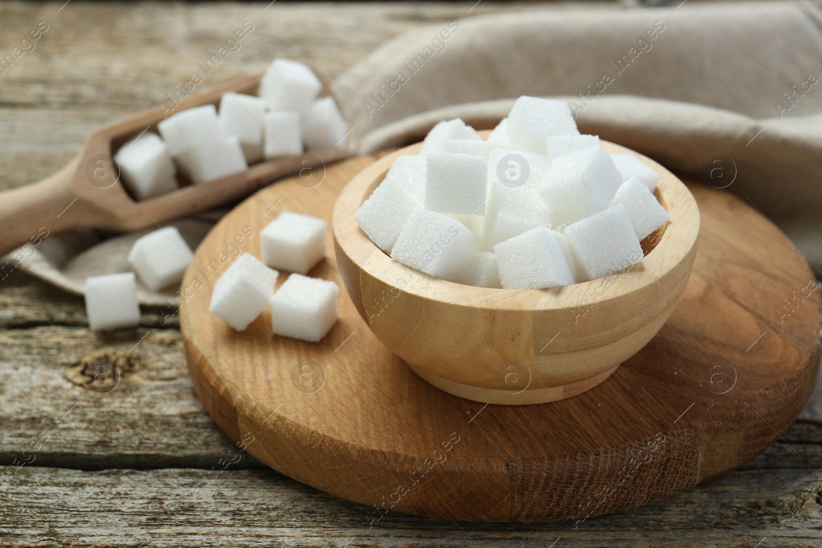 Photo of White sugar cubes in bowl and scoop on wooden table, closeup