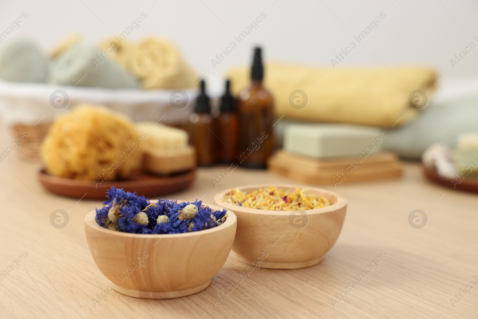Photo of Bowls with dry flowers on light wooden table. Spa therapy