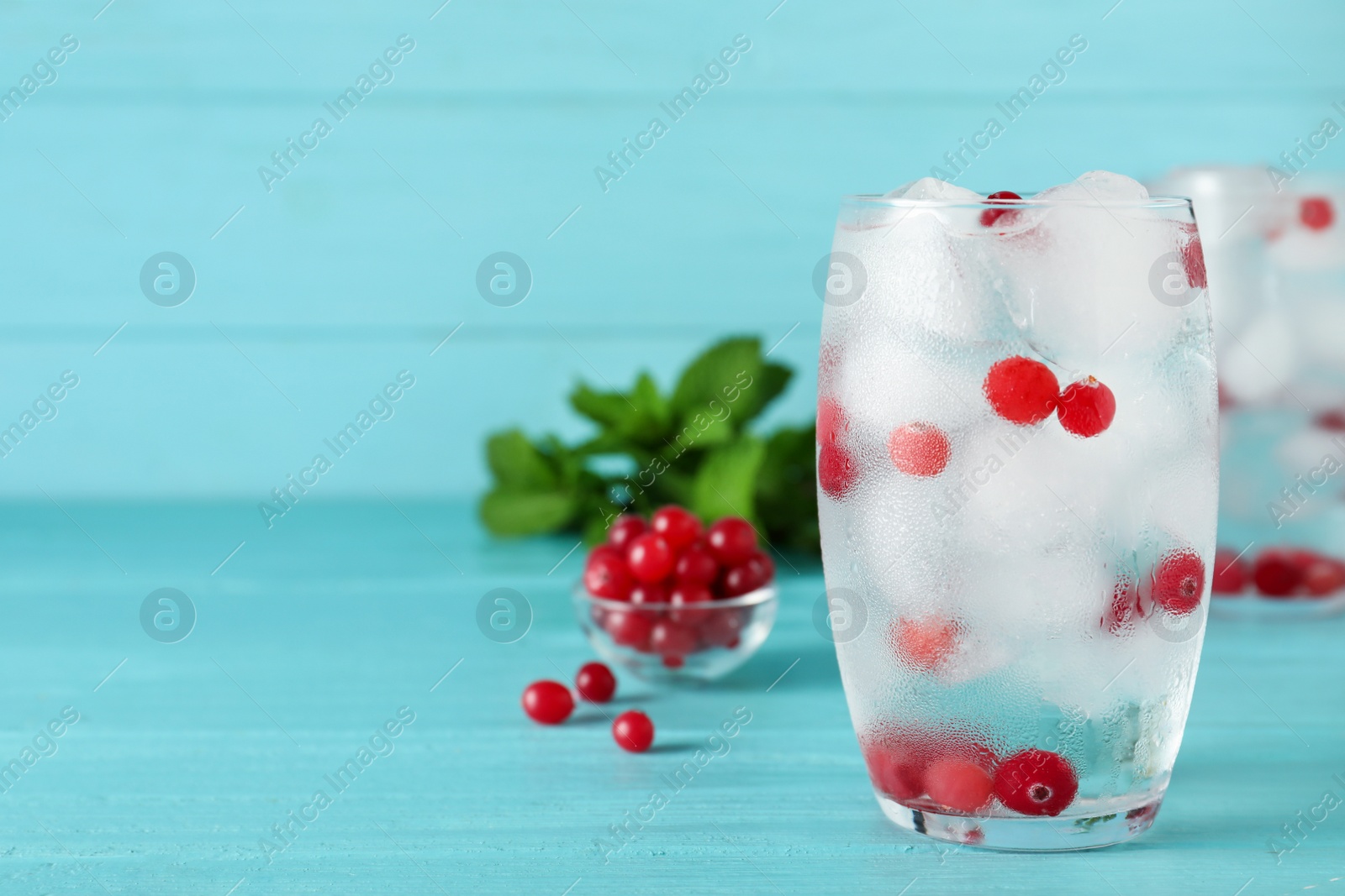 Photo of Glass of cocktail with vodka, ice and cranberry on blue wooden table. Space for text