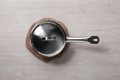 Photo of Steel saucepan with strainer lid on light wooden table, top view