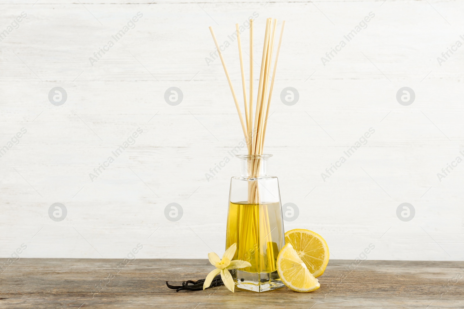 Photo of Aromatic reed freshener, lemon and vanilla on wooden table against light background. Space for text