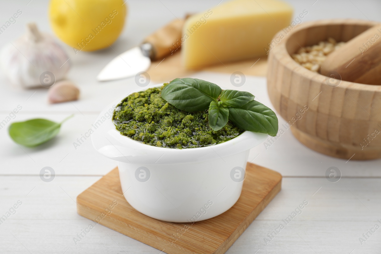Photo of Delicious pesto sauce in bowl and ingredients on white wooden table, closeup