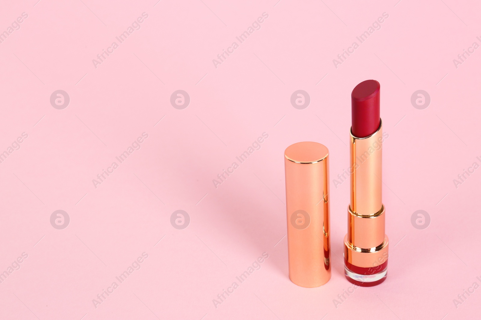 Photo of Bright lipstick in gold tube on pink background, space for text