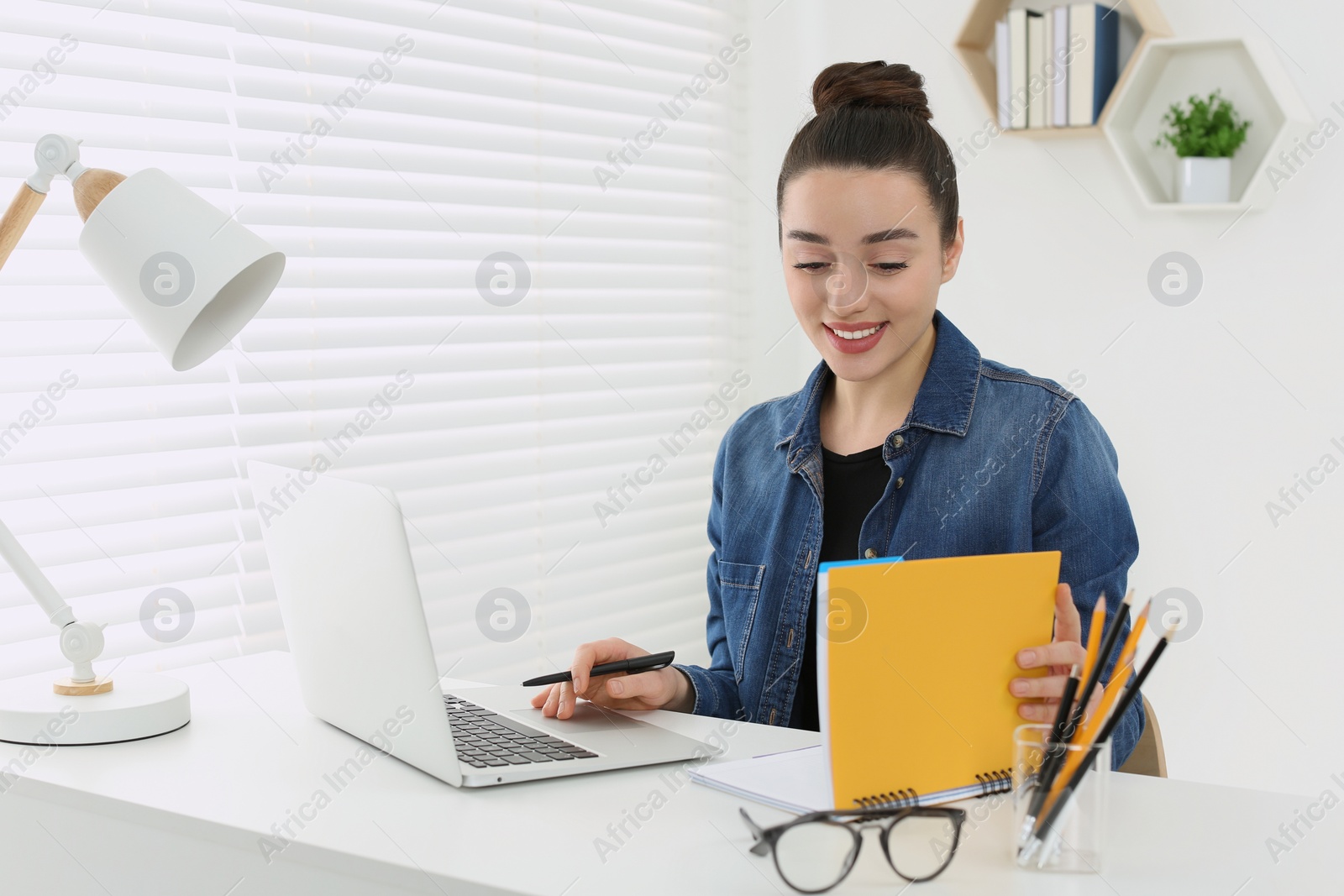 Photo of Home workplace. Happy woman looking at notebook at white desk in room