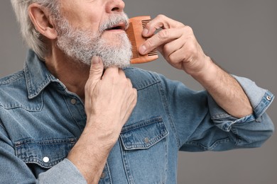 Man combing beard on grey background, closeup