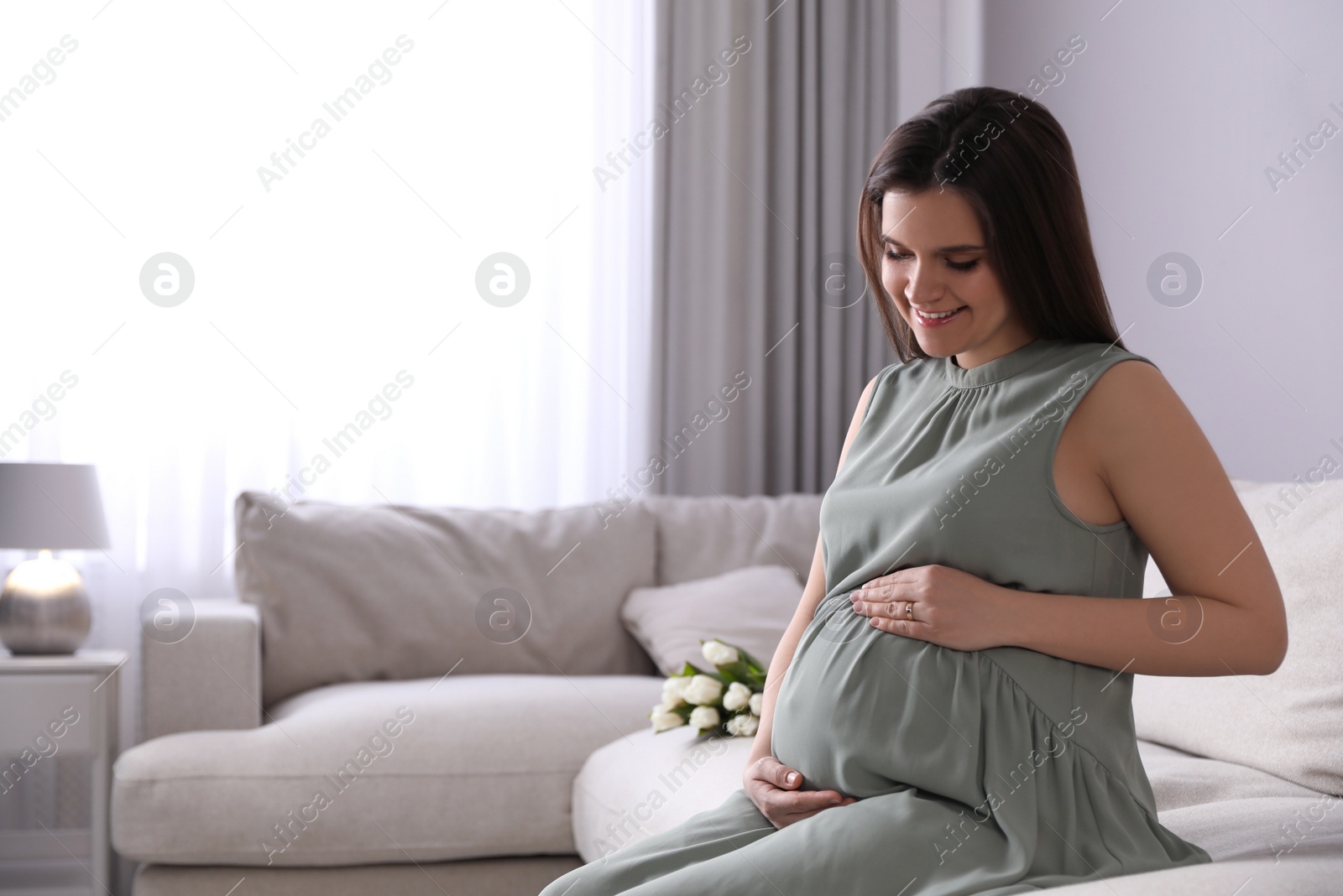 Photo of Young pregnant woman sitting on sofa at home