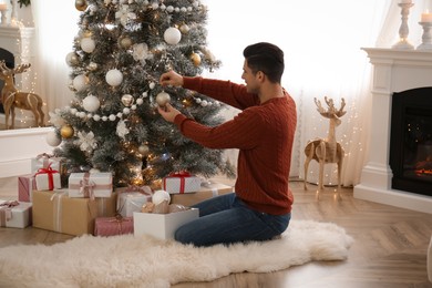 Man decorating Christmas tree in beautiful room interior