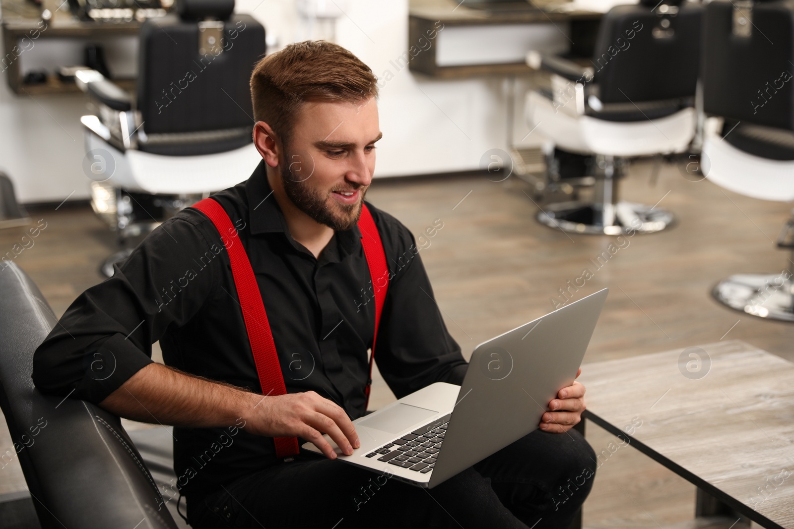 Photo of Young business owner working with laptop in barber shop