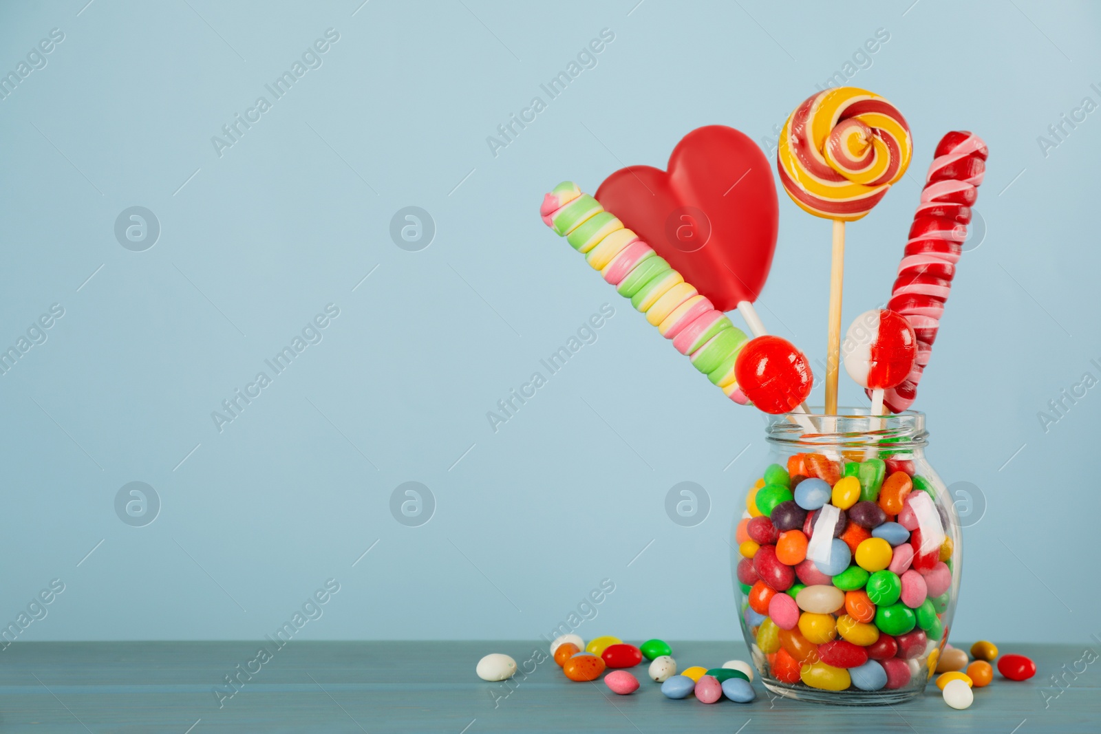 Photo of Jar with different delicious candies on turquoise wooden table, space for text