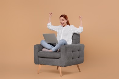 Photo of Happy young woman with laptop sitting in armchair on beige background