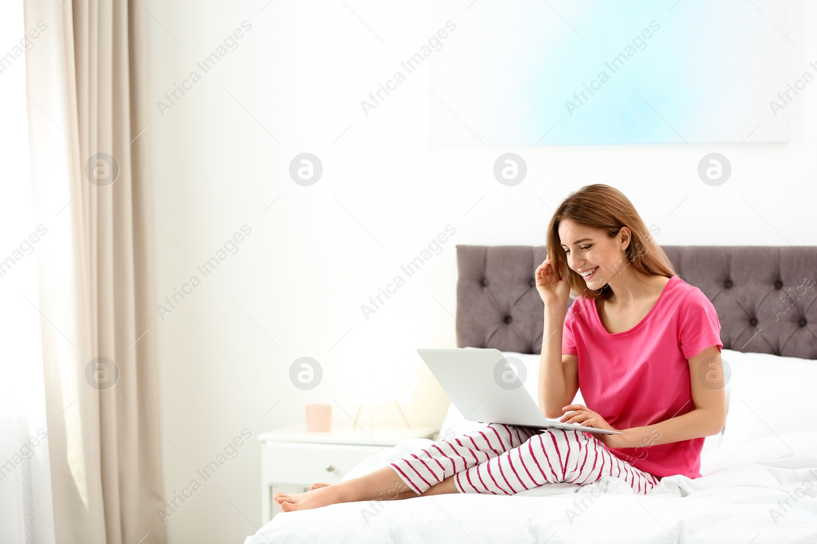 Photo of Young woman using modern laptop in bedroom