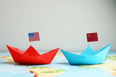 Paper boats with USA and China flags on world map against light background. Trade war concept
