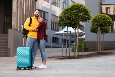 Photo of Long-distance relationship. Beautiful young couple with luggage hugging outdoors