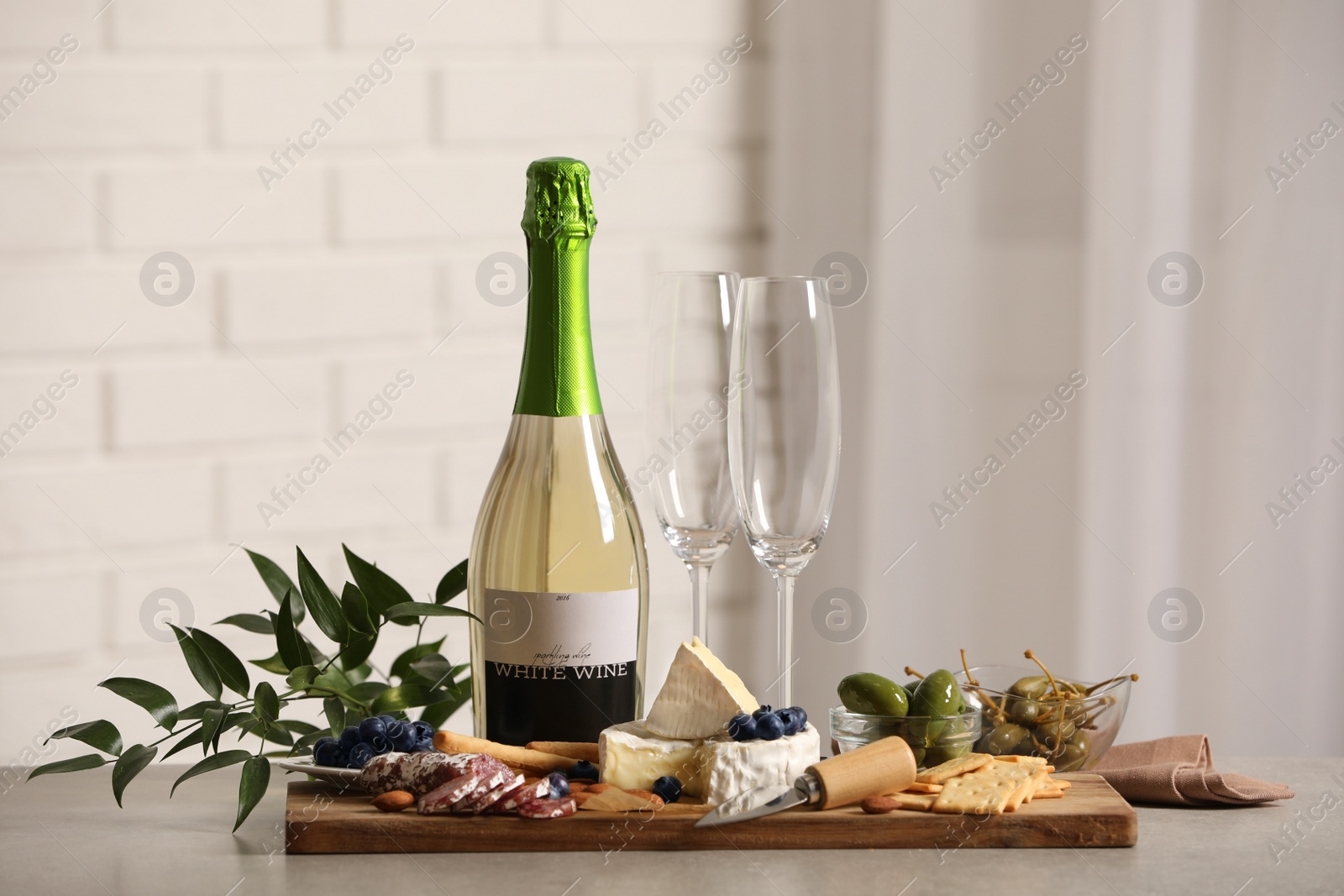 Photo of Bottle of white wine, glasses and delicious snacks on grey table indoors