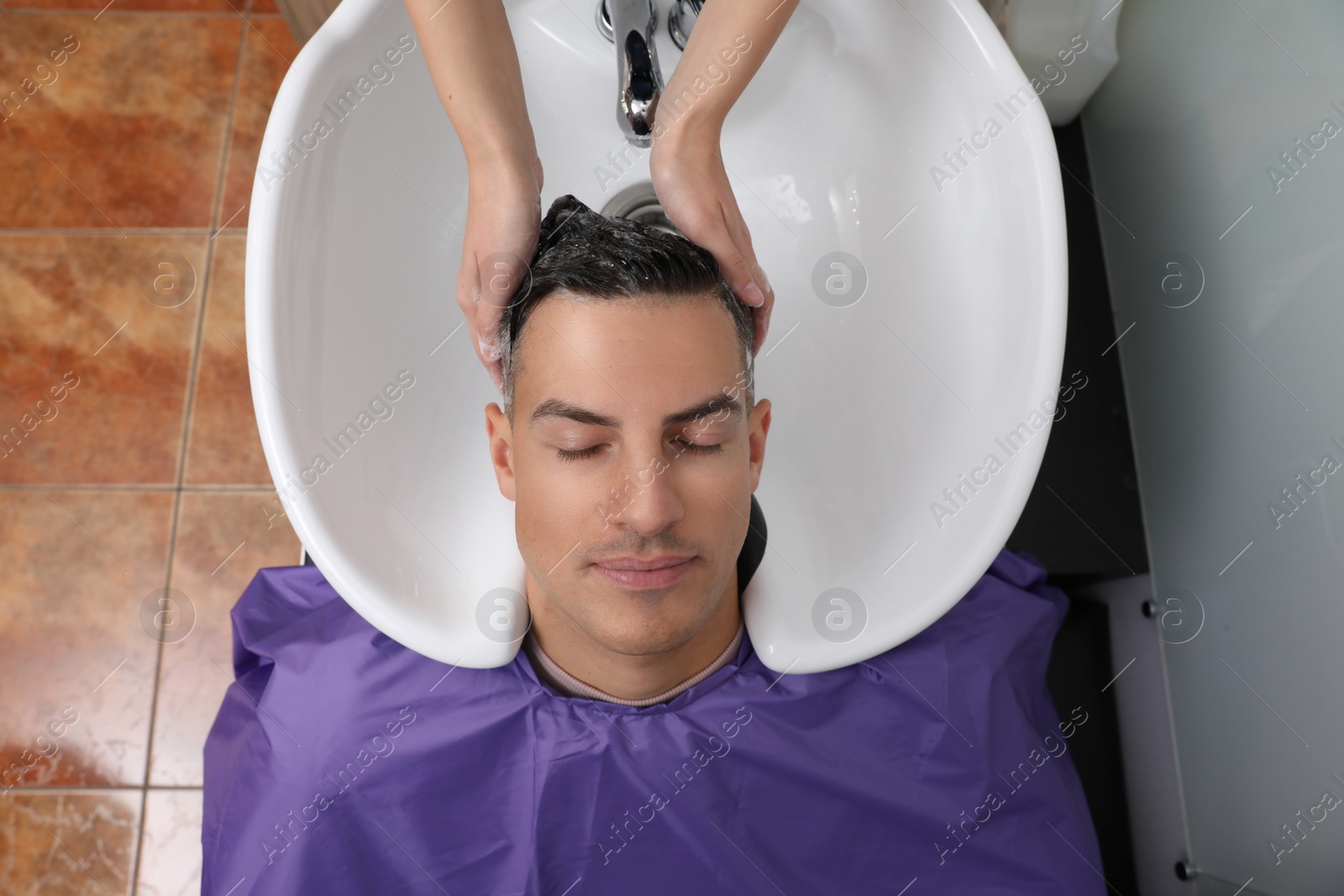 Photo of Professional hairdresser washing client's hair at sink in salon, top view