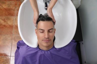 Photo of Professional hairdresser washing client's hair at sink in salon, top view