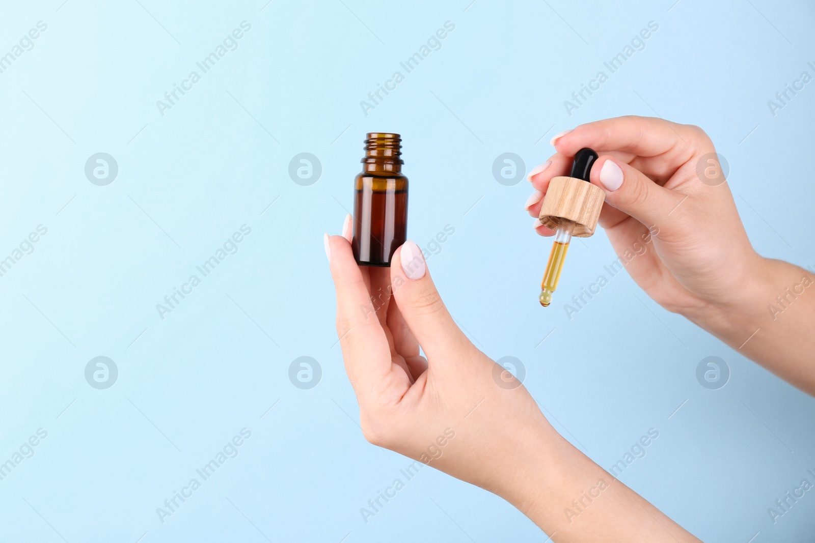 Photo of Woman applying essential oil onto wrist against light blue background, closeup. Space for text