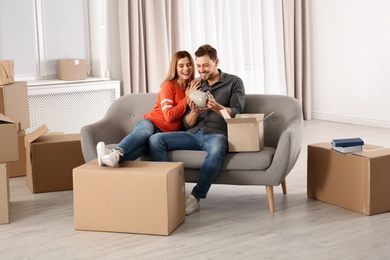 Photo of Couple unpacking cardboard box while resting on sofa in their new house. Moving day