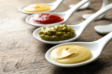 Photo of Spoons with different sauces on wooden background
