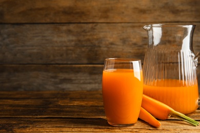 Photo of Jug and glass of freshly made carrot juice on wooden table, space for text