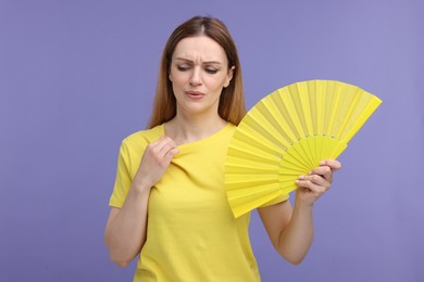 Photo of Beautiful woman waving yellow hand fan to cool herself on violet background