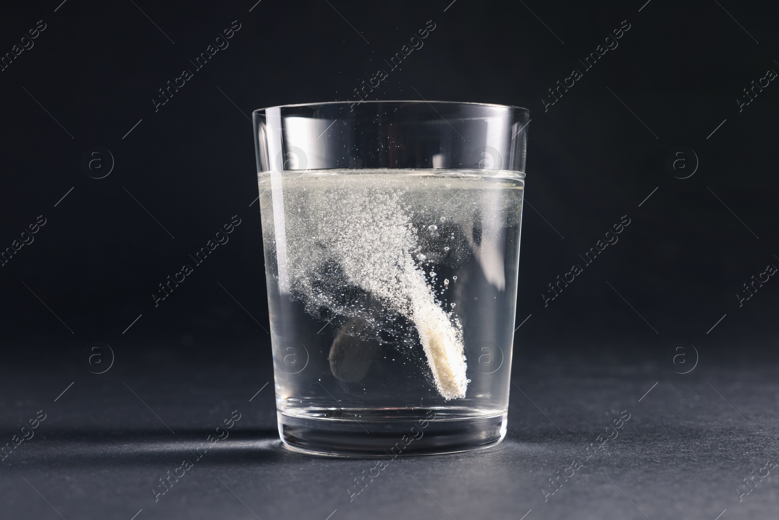 Photo of Effervescent pill dissolving in glass of water on grey table