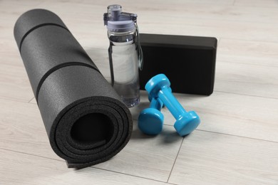 Photo of Exercise mat, yoga block, dumbbells and bottle of water on light wooden floor