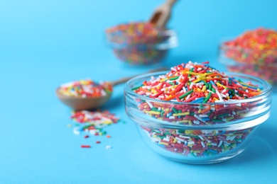 Photo of Colorful sprinkles in bowl on light blue background, closeup with space for text. Confectionery decor