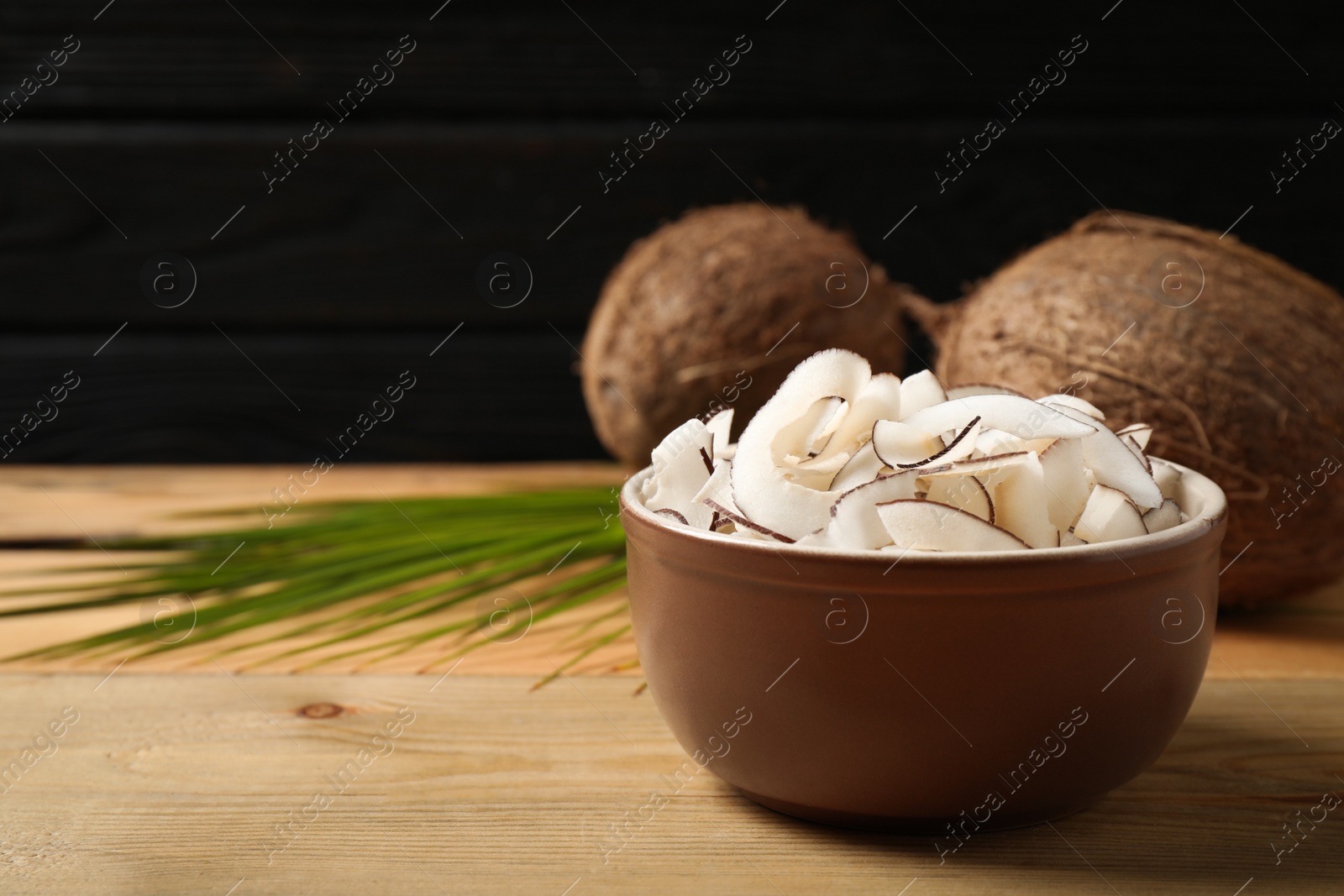 Photo of Tasty coconut chips on wooden table against black background. Space for text