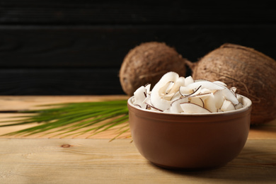 Photo of Tasty coconut chips on wooden table against black background. Space for text
