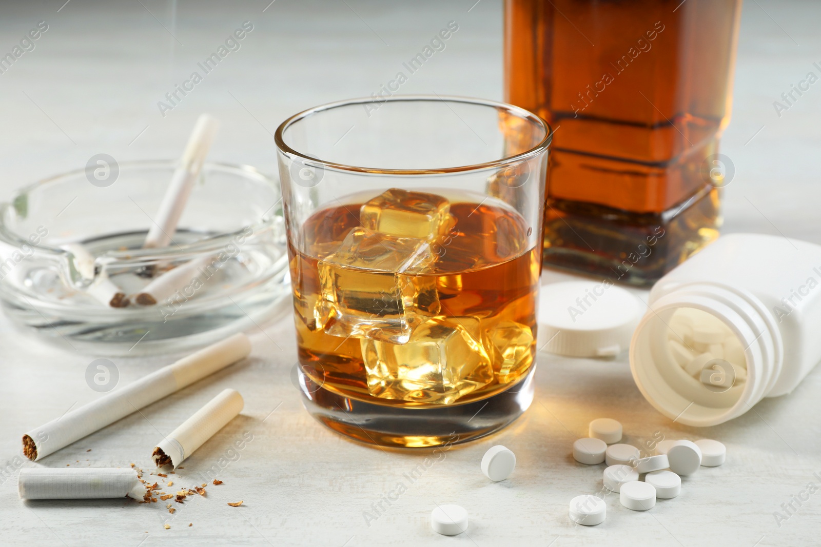 Photo of Alcohol and drug addiction. Whiskey in glass, cigarettes and pills on white table