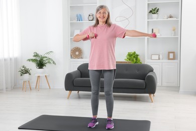 Senior woman exercising with dumbbells on mat at home. Sports equipment