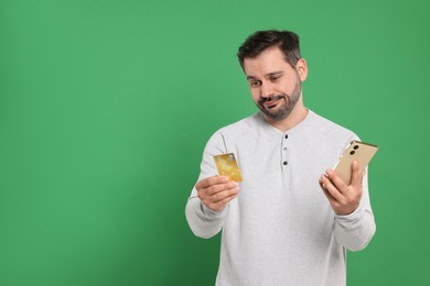 Confused man with credit card and smartphone on green background, space for text. Debt problem