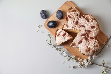 Photo of Board with cut delicious Italian Easter dove cake (traditional Colomba di Pasqua), painted eggs and flowering branches on light grey table, flat lay. Space for text