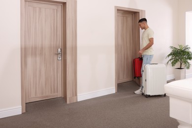 Photo of Happy man with suitcases in hotel corridor
