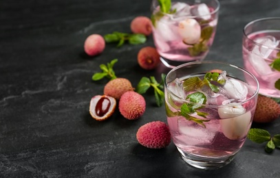 Photo of Delicious lychee cocktails with mint and fresh fruits on black table. Space for text