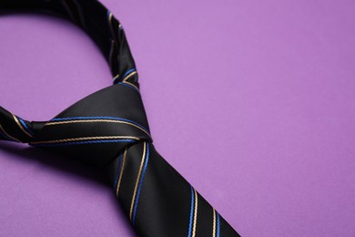 Striped necktie on purple background, closeup. Space for text
