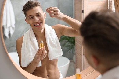 Handsome man applying serum onto his face in bathroom