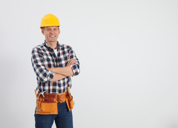 Handsome carpenter with tool belt on light background. Space for text