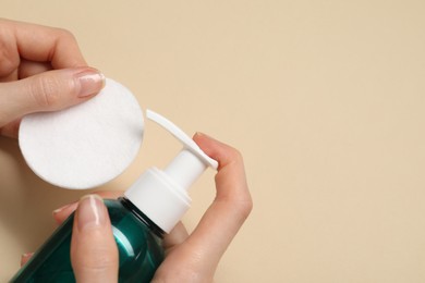 Photo of Woman applying makeup remover onto cotton pad on beige background, top view. Space for text