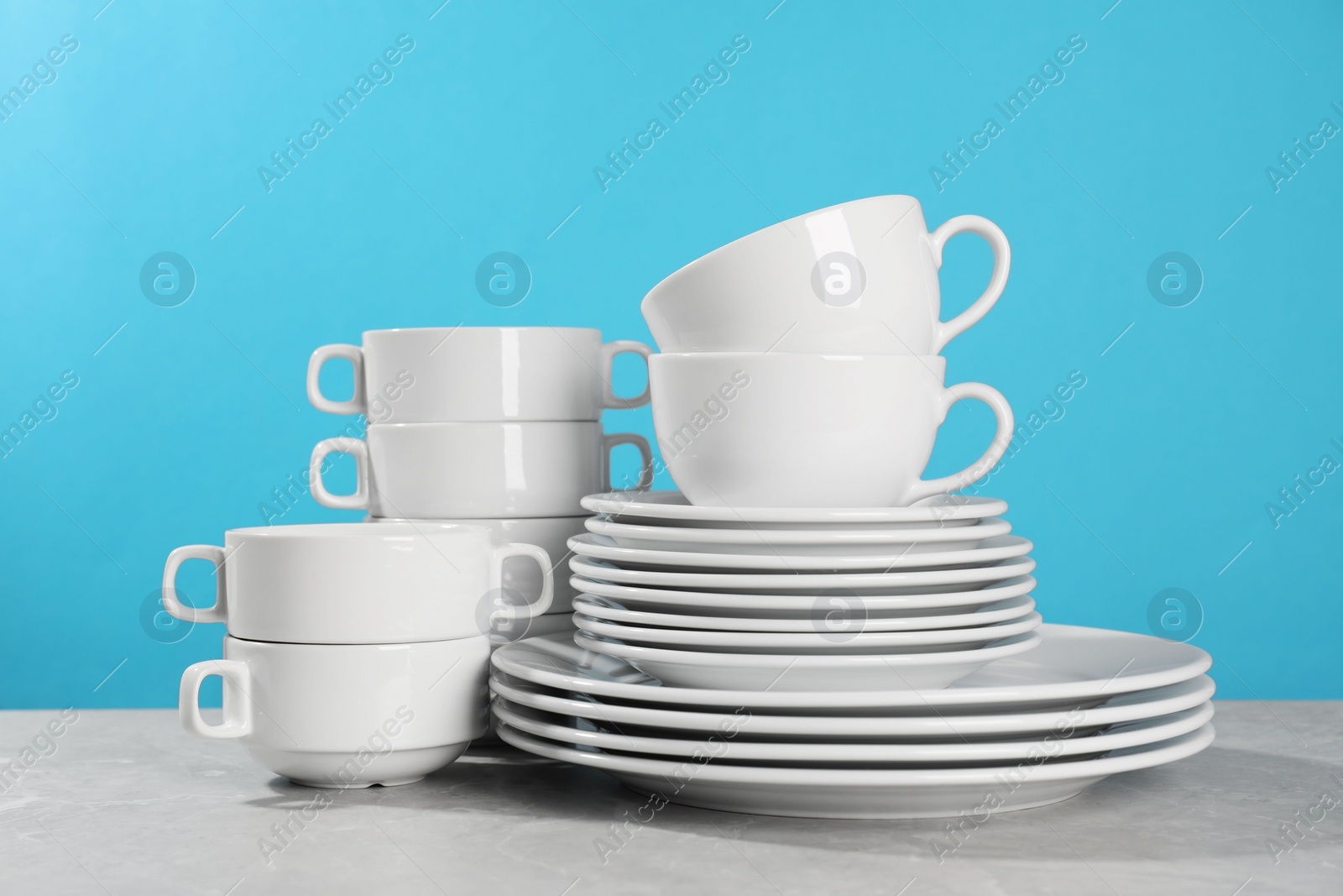 Photo of Set of clean dishware on grey table against light blue background