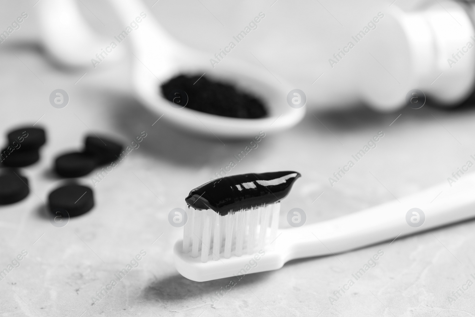 Photo of Brush with charcoal toothpaste on light grey table, closeup