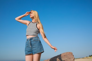 Photo of Beautiful young woman against blue sky on sunny day, space for text