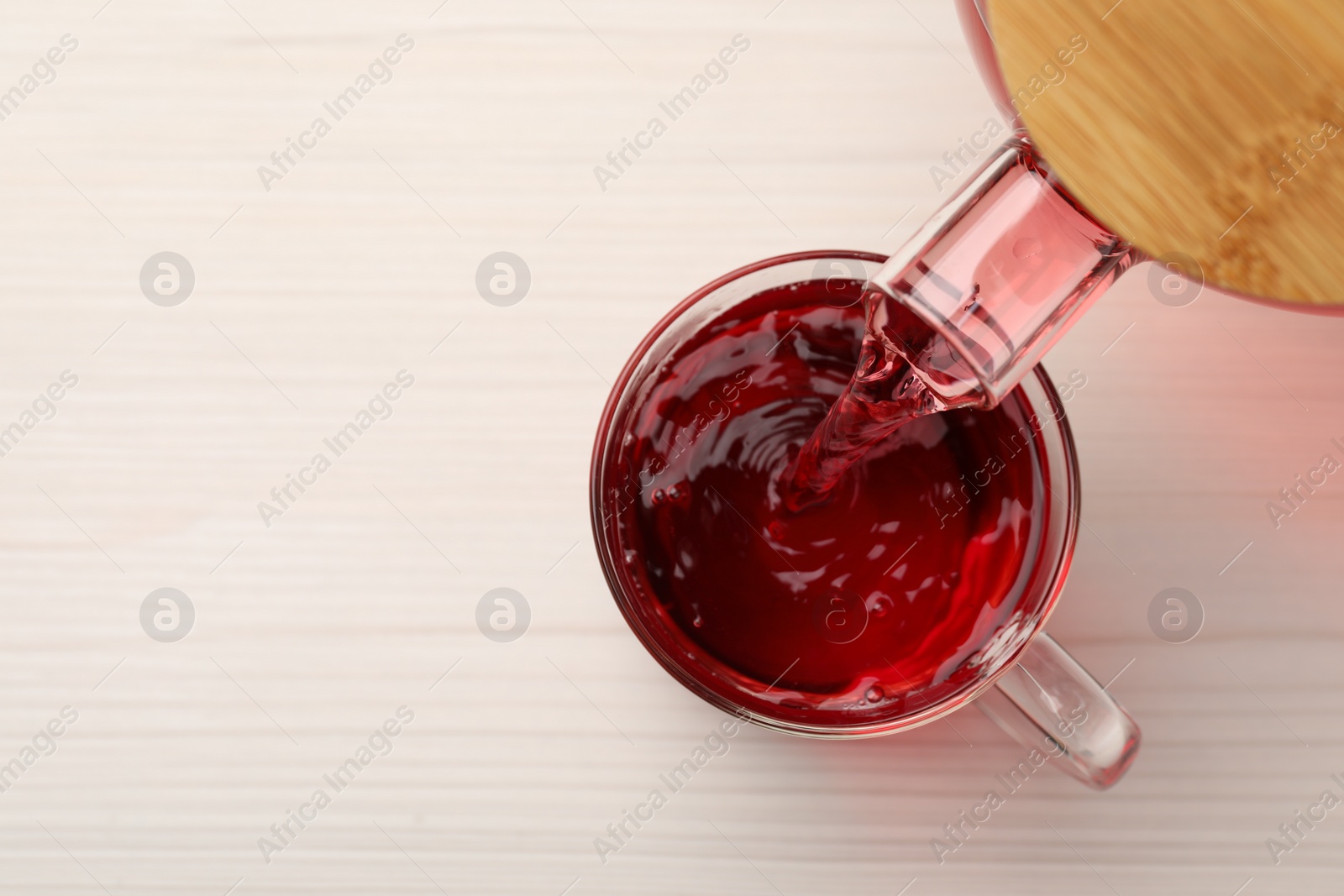 Photo of Pouring delicious hibiscus tea into cup on white wooden table, top view. Space for text