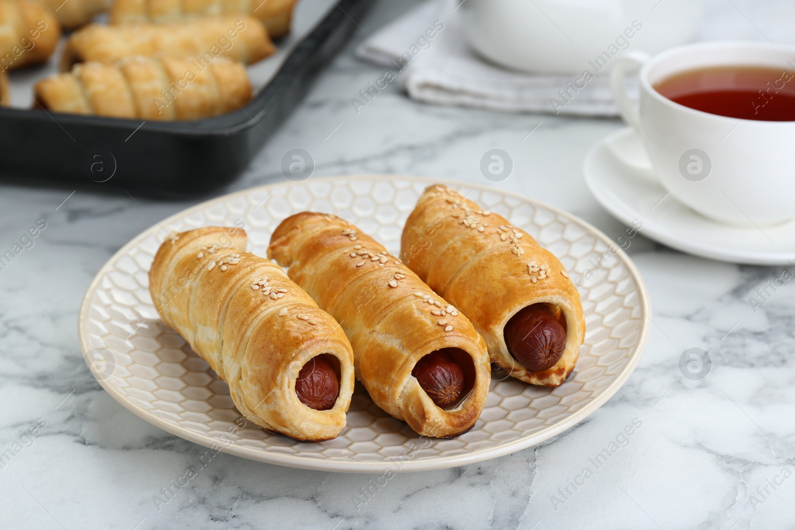 Photo of Delicious sausage rolls and hot drink on white marble table